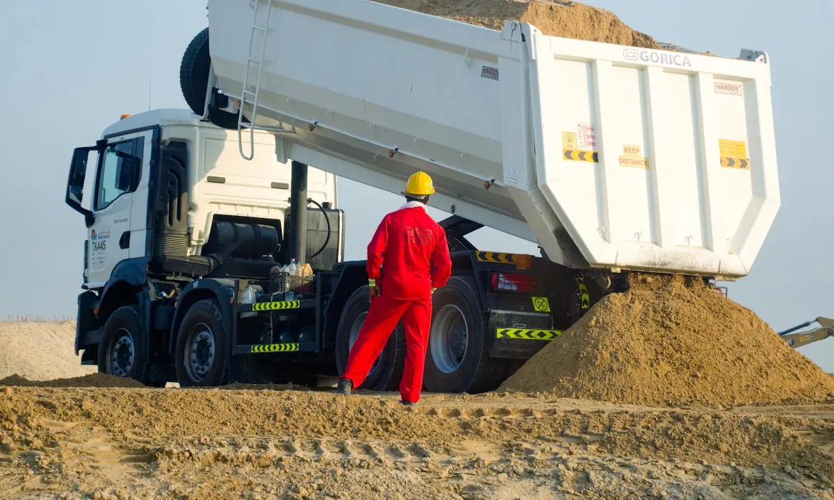 Site worker directing a bulk sand delivery from a tipper truck